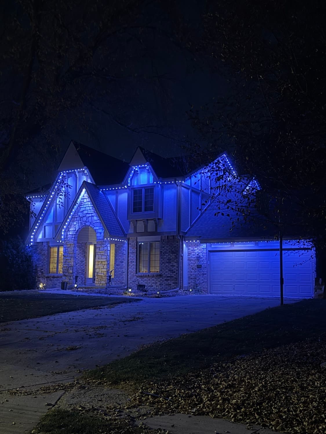 Tudor-style home lit in deep blue permanent lighting along every roofline and peak.