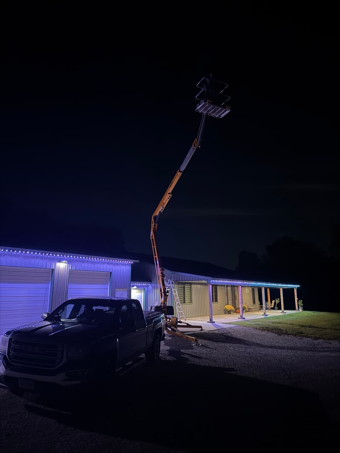 Hound Lighting crew installing permanent lighting from a bucket lift on a lit building at night.